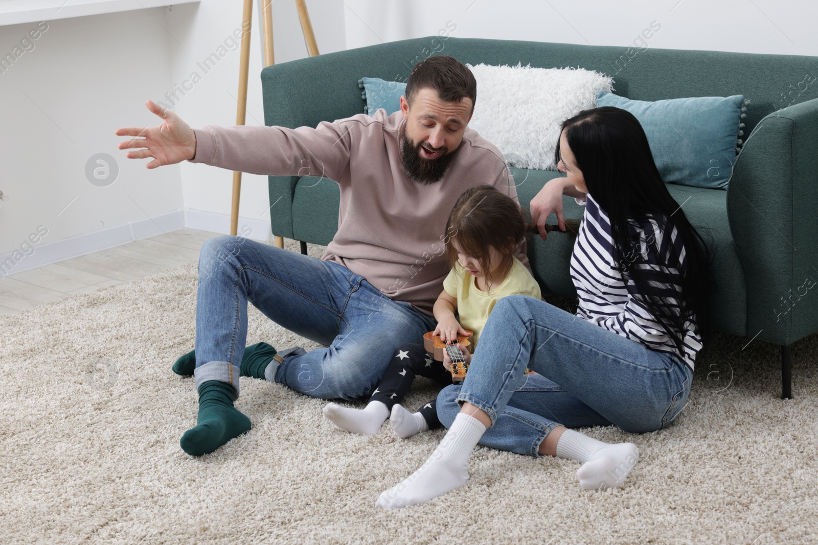 Photo of Parents and their cute little daughter playing ukulele at home