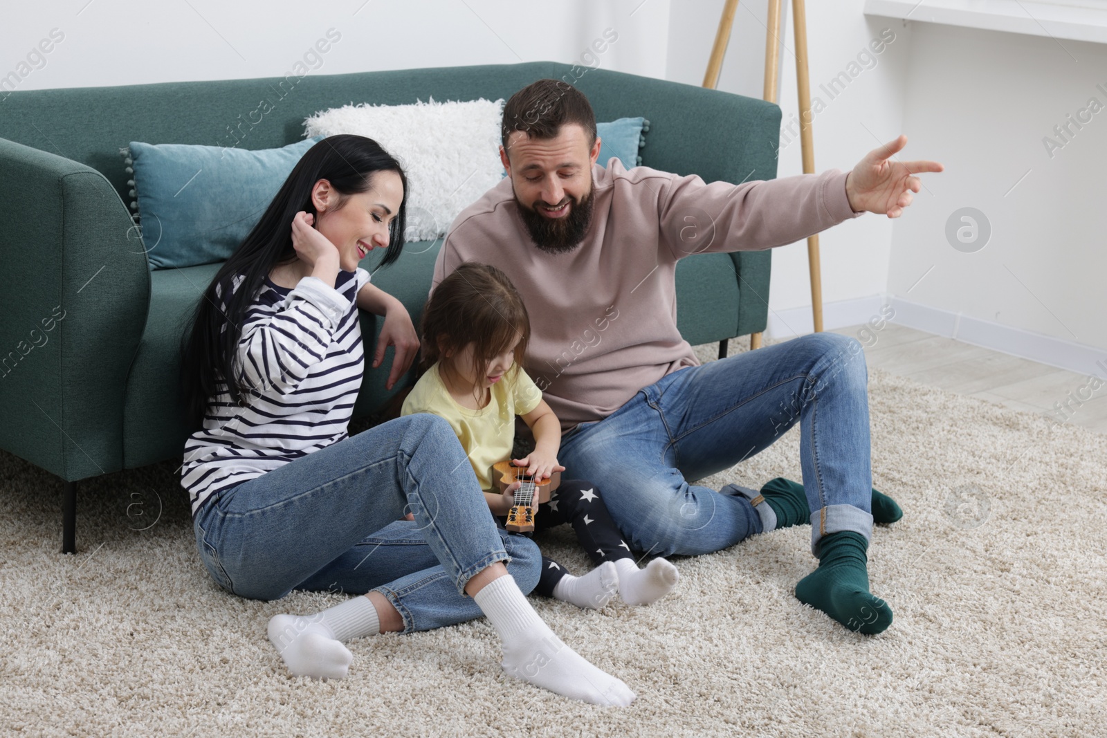 Photo of Parents and their cute little daughter playing ukulele at home