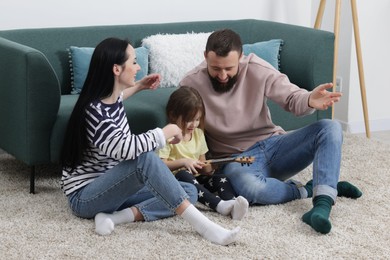 Photo of Parents and their cute little daughter playing ukulele at home