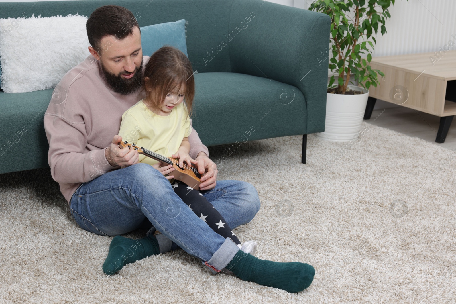 Photo of Father and his cute little daughter playing ukulele at home