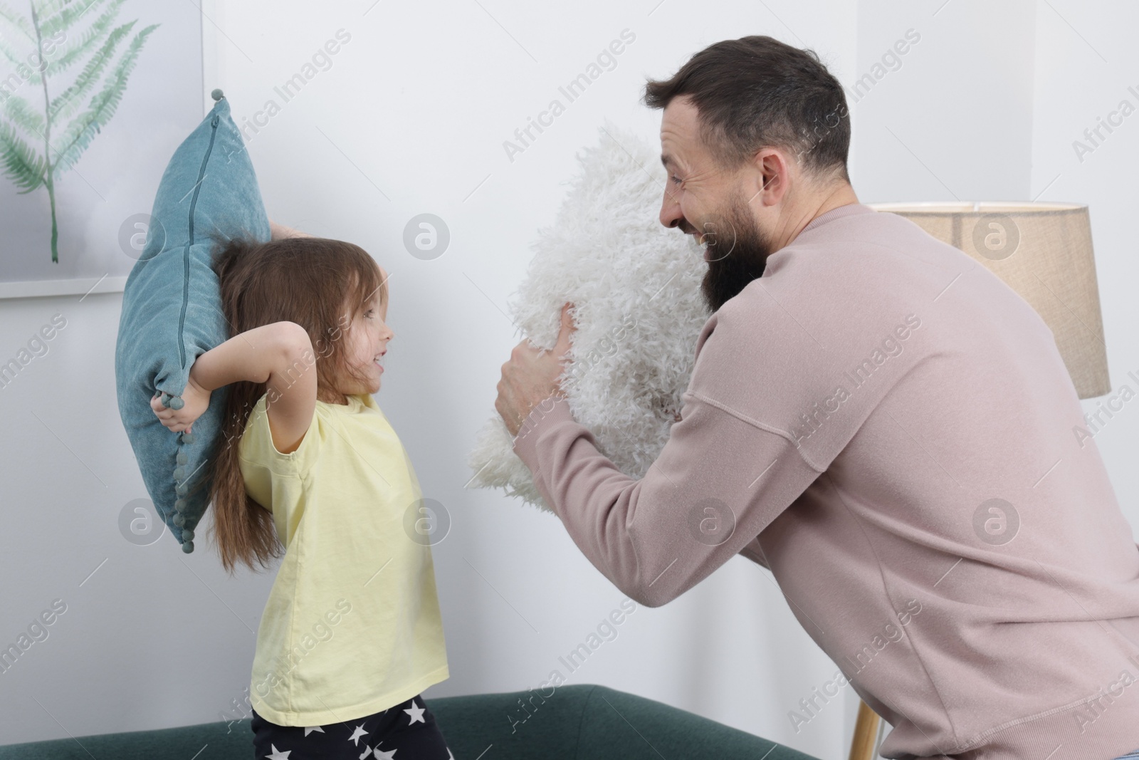 Photo of Cute little girl and her father having fun while fighting with pillows at home