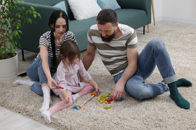 Photo of Cute little girl and her parents playing with set of colorful figures at home