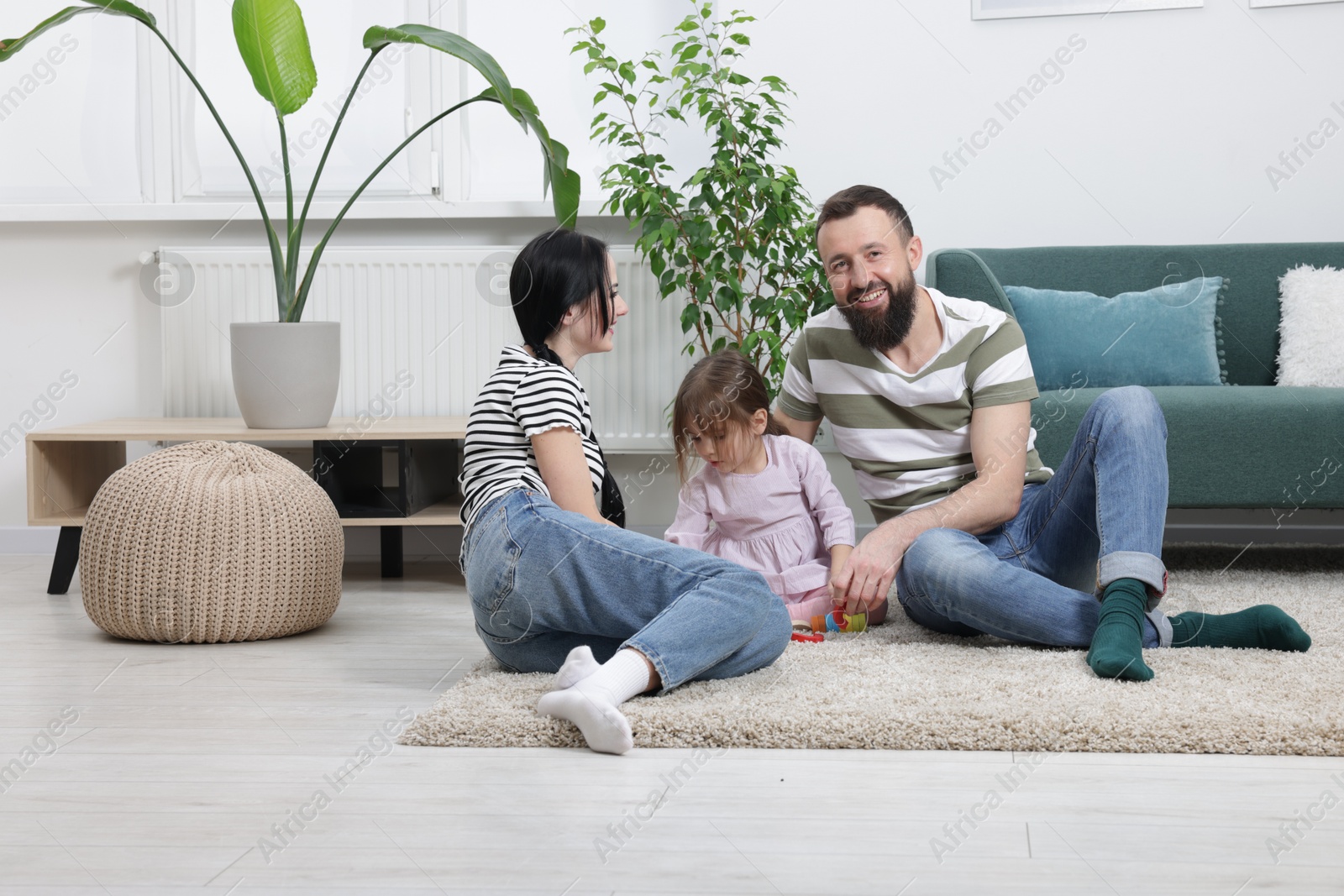 Photo of Cute little girl and her parents playing with set of colorful figures at home