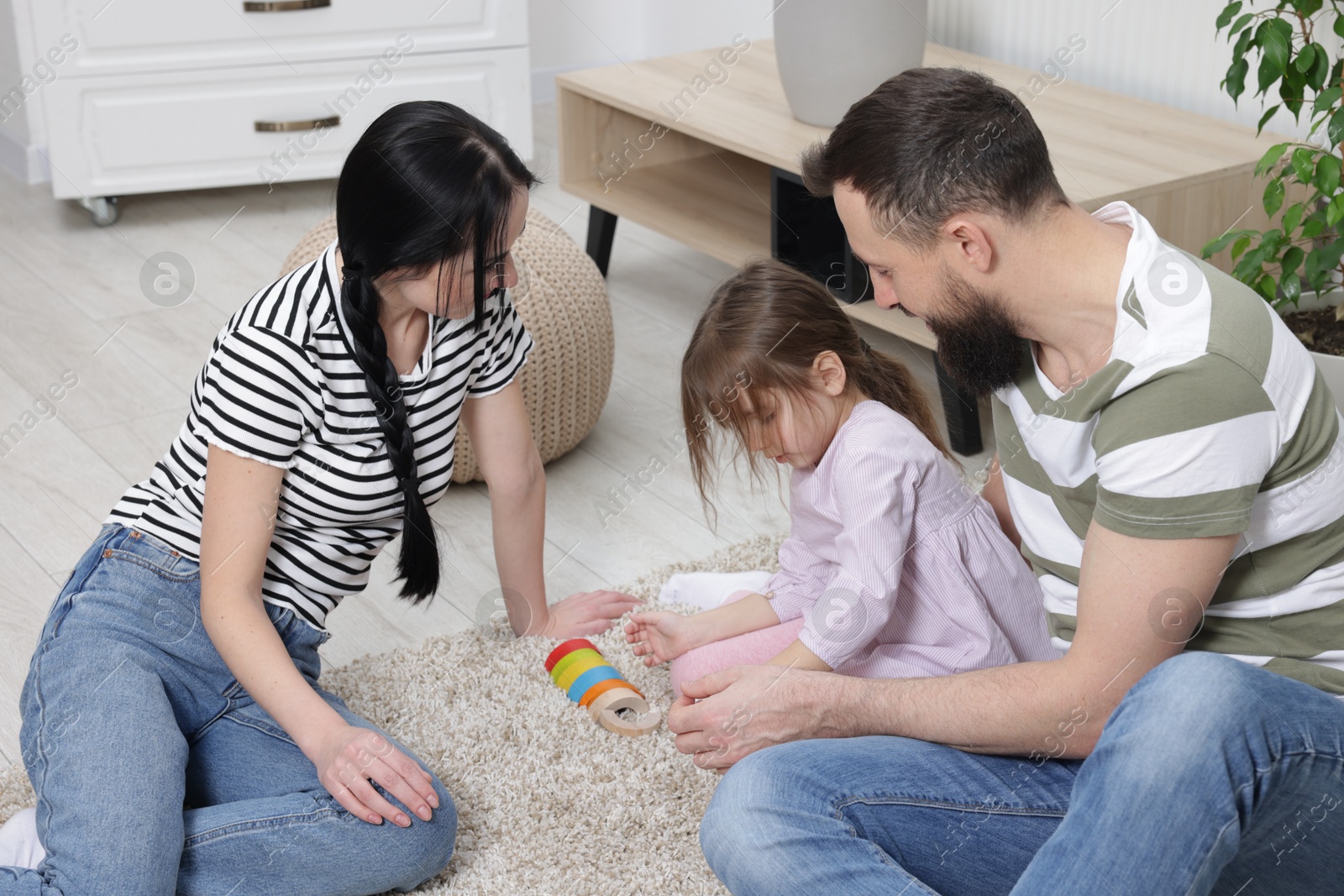 Photo of Cute little girl and her parents playing with set of colorful figures at home