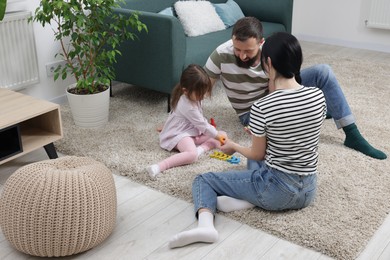 Photo of Cute little girl and her parents playing with set of colorful figures at home