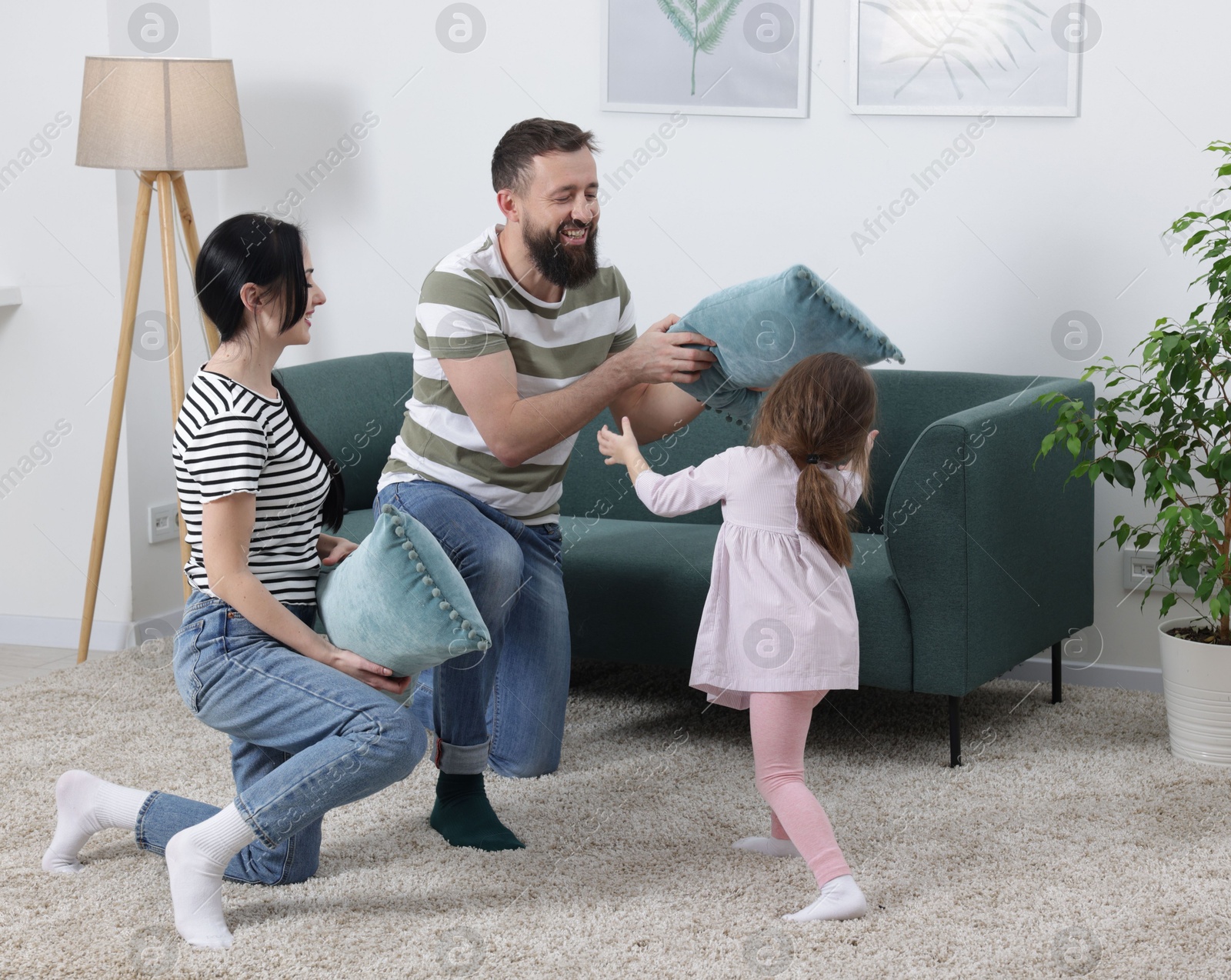 Photo of Cute little girl and her parents having fun while fighting with pillows at home