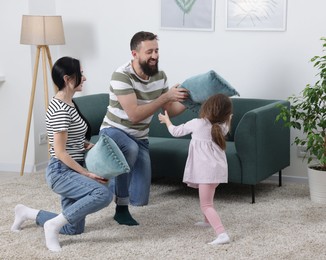 Photo of Cute little girl and her parents having fun while fighting with pillows at home