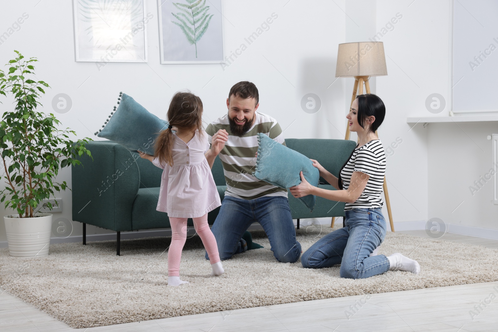 Photo of Cute little girl and her parents having fun while fighting with pillows at home