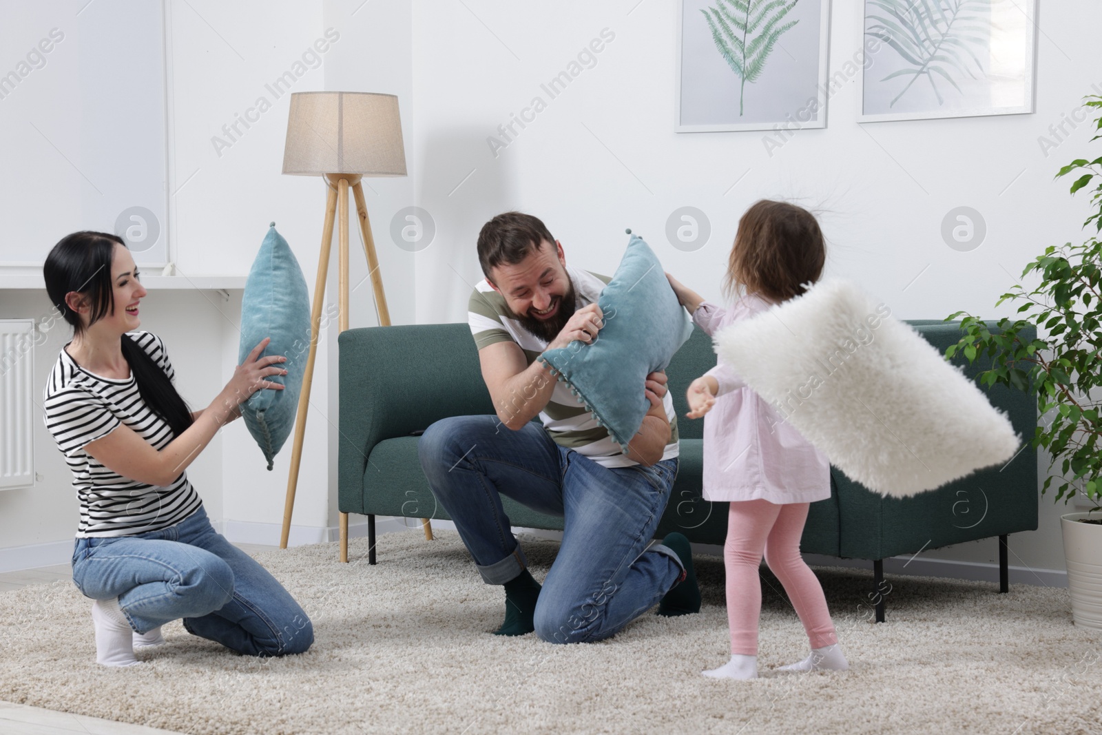 Photo of Cute little girl and her parents having fun while fighting with pillows at home