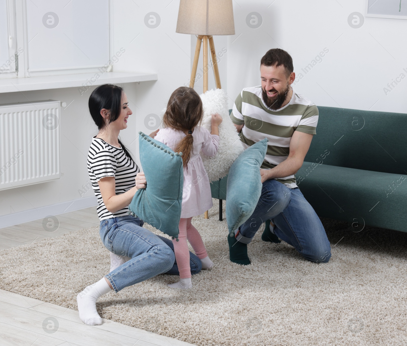 Photo of Cute little girl and her parents having fun while fighting with pillows at home