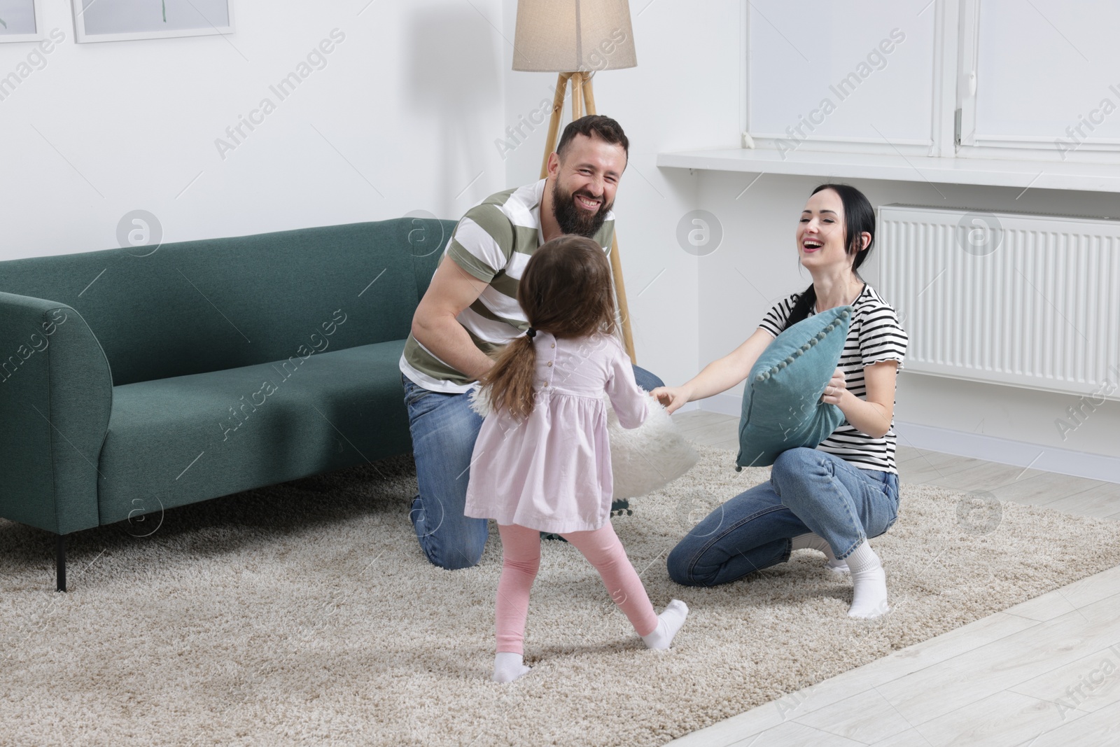 Photo of Cute little girl and her parents having fun while fighting with pillows at home