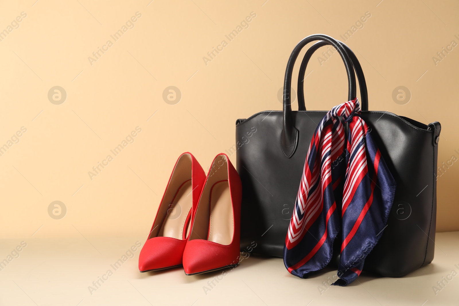 Photo of Leather bag with handkerchief and high heeled shoes on beige background. Space for text