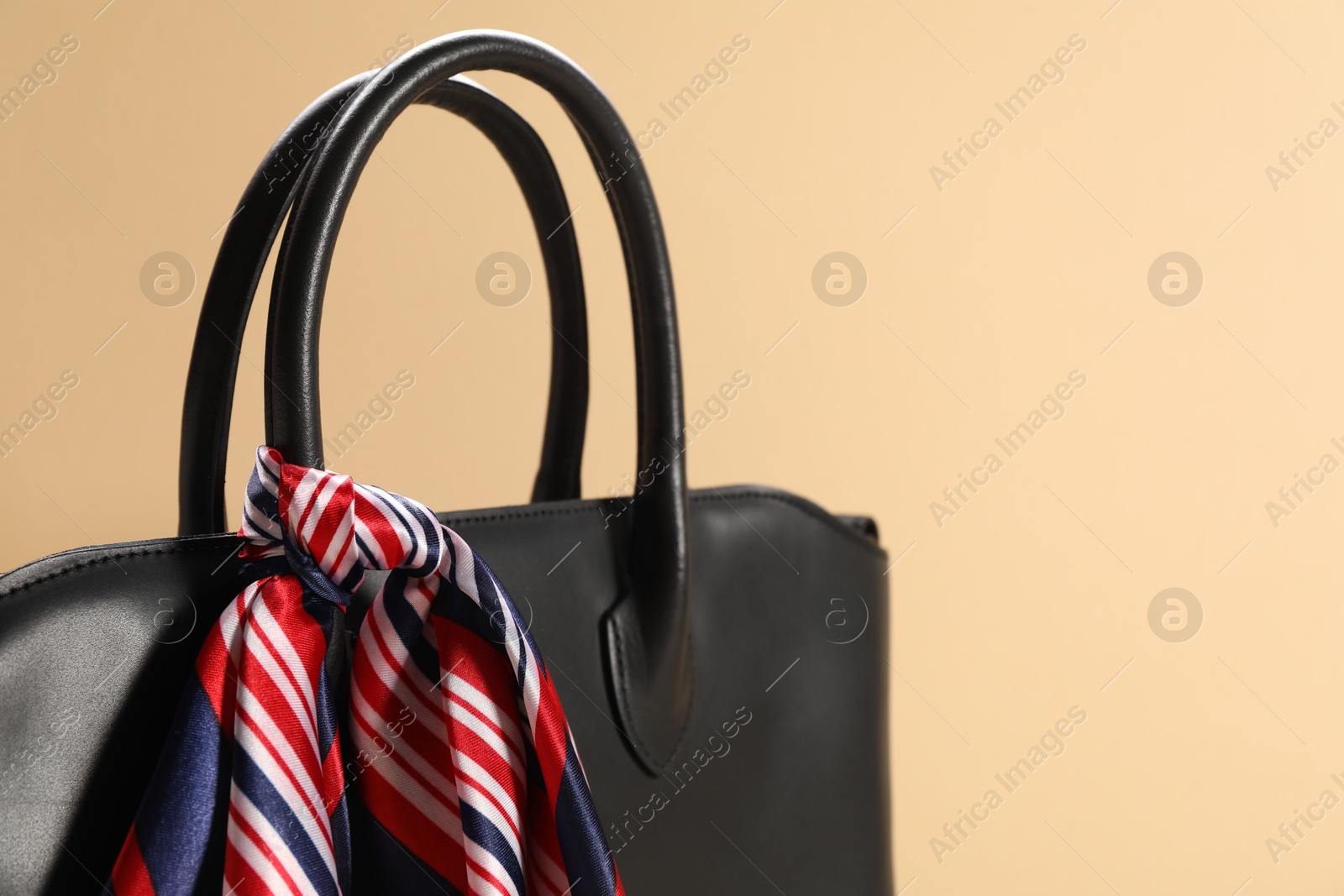 Photo of Leather bag with handkerchief on beige background, closeup. Space for text