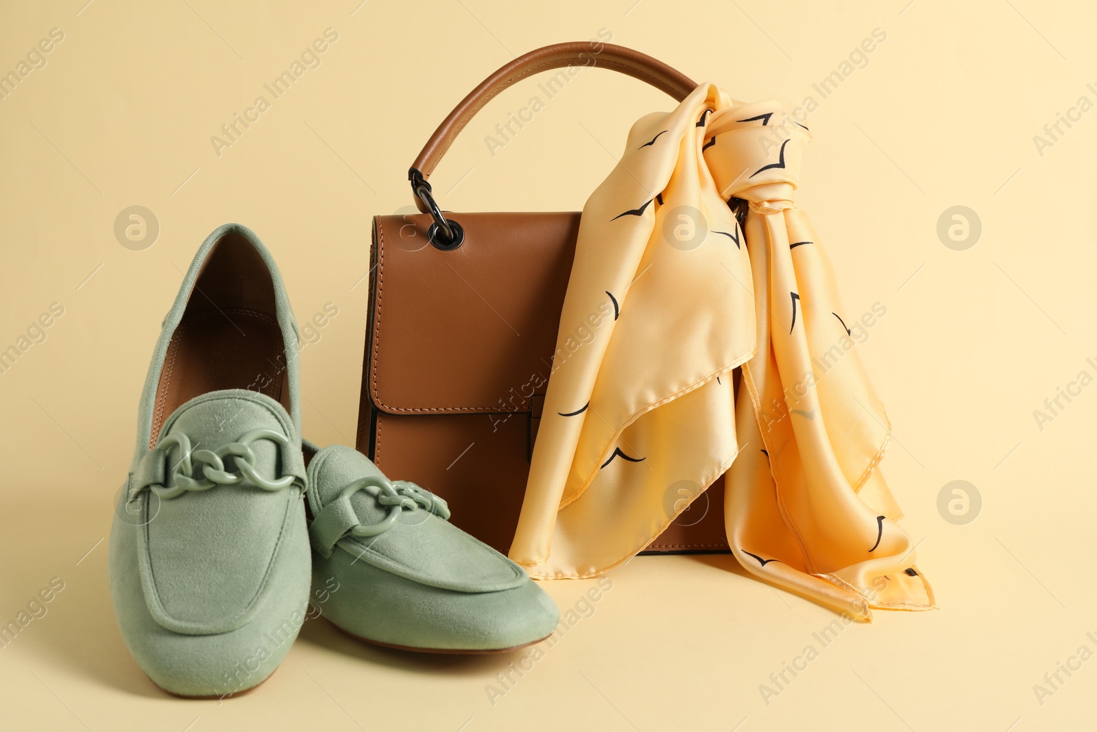 Photo of Leather bag with handkerchief and loafers on beige background, closeup