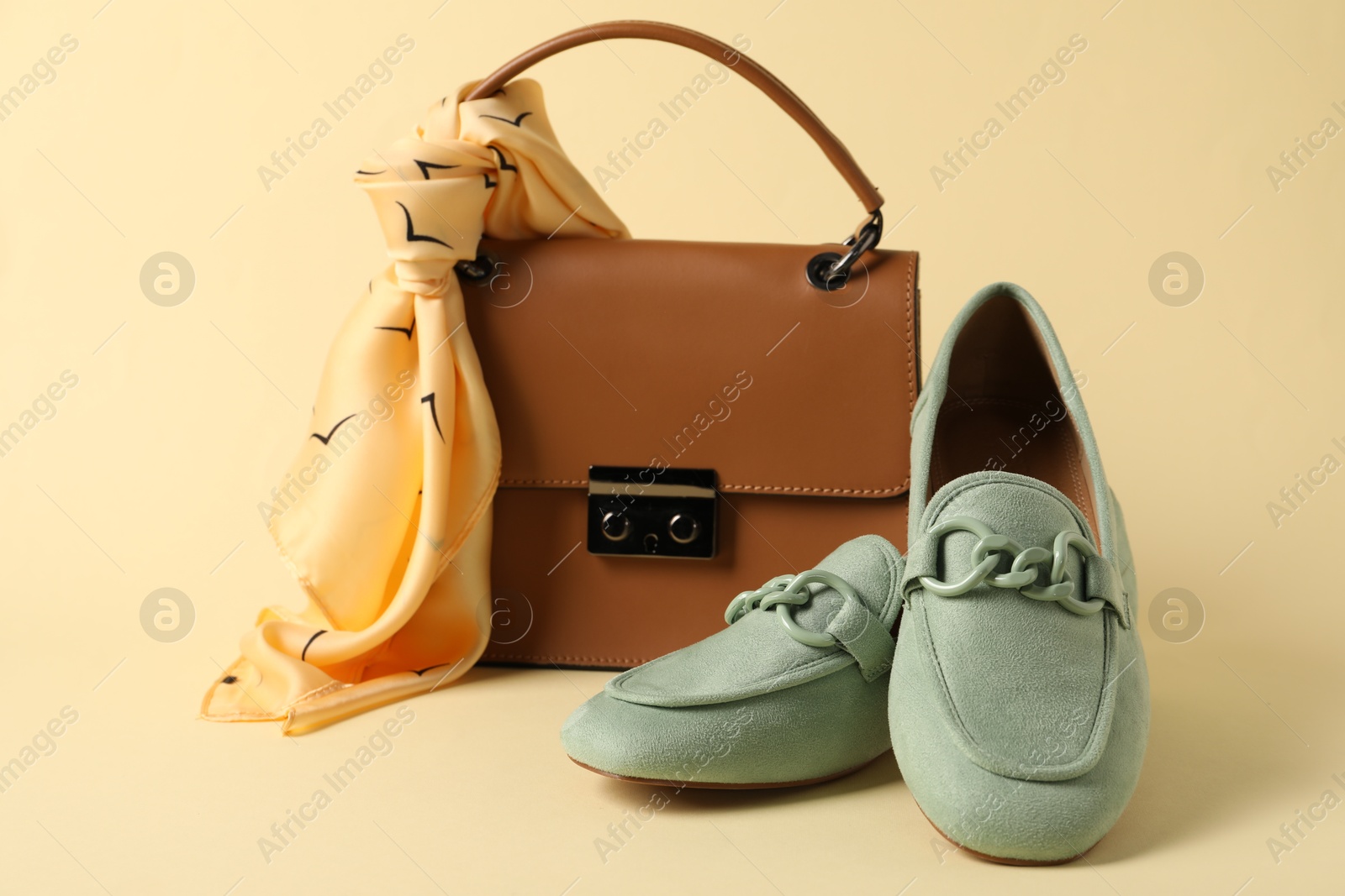 Photo of Leather bag with handkerchief and loafers on beige background, closeup