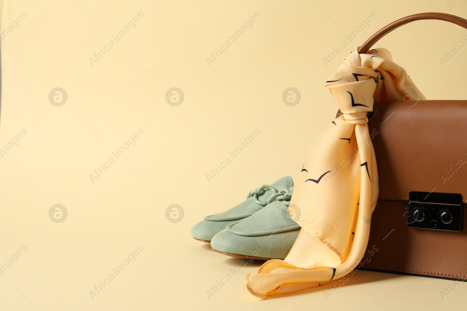 Photo of Leather bag with handkerchief and loafers on beige background, closeup. Space for text