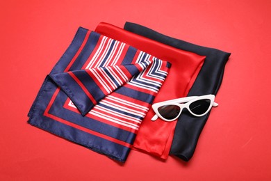 Photo of Stylish handkerchiefs and sunglasses on red background, top view