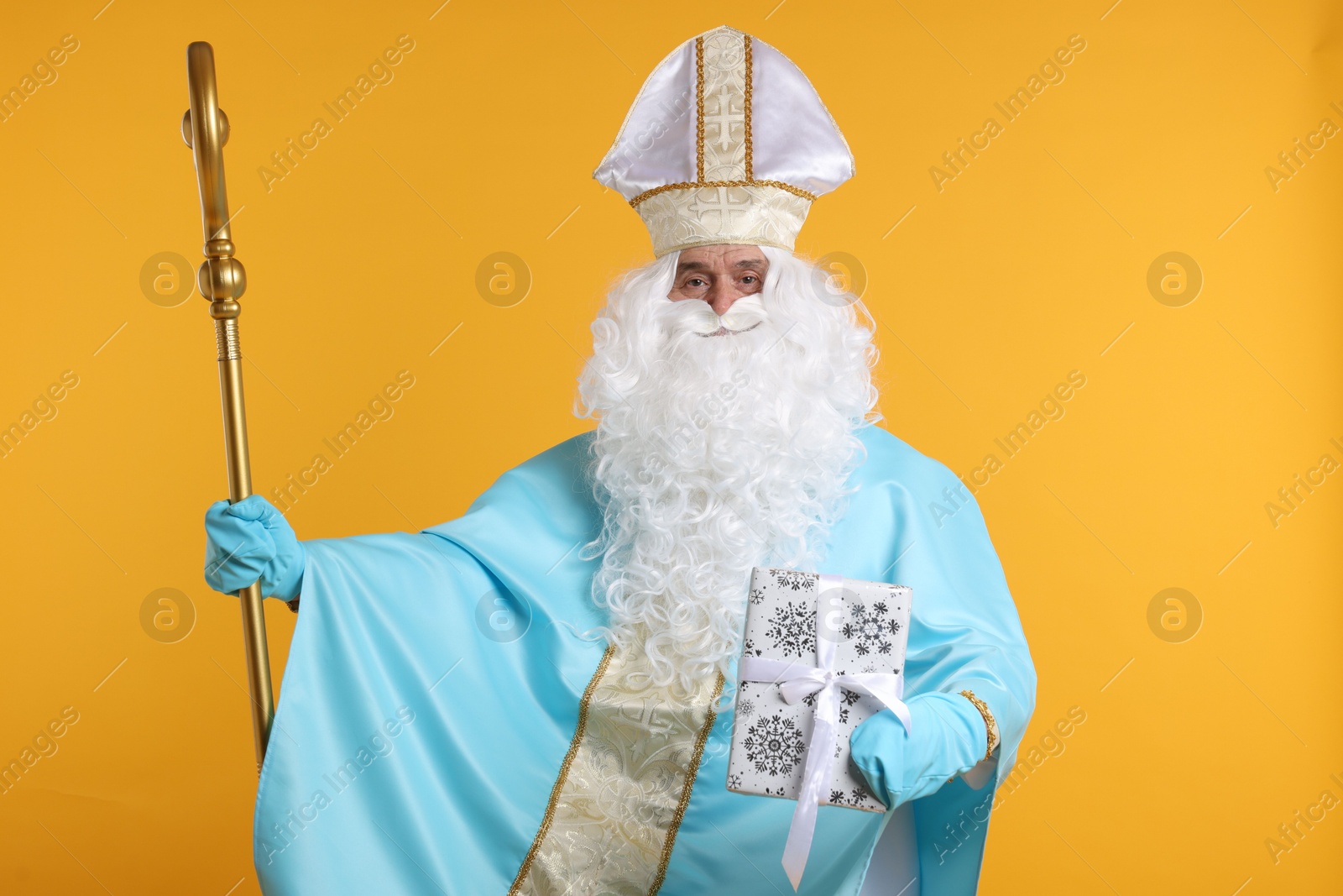 Photo of Saint Nicholas with Christmas gift and crozier on orange background