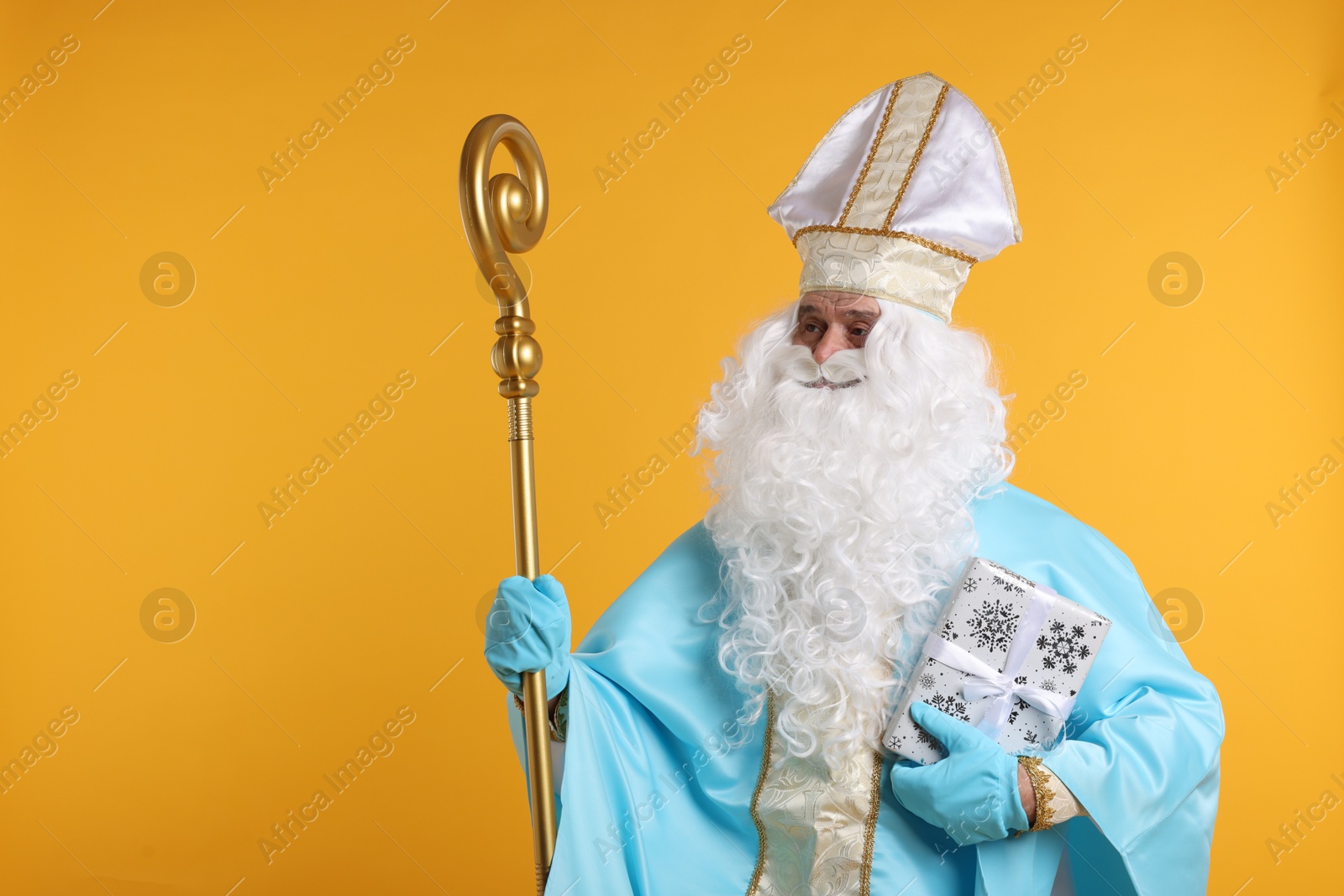 Photo of Saint Nicholas with Christmas gift and crozier on orange background, space for text