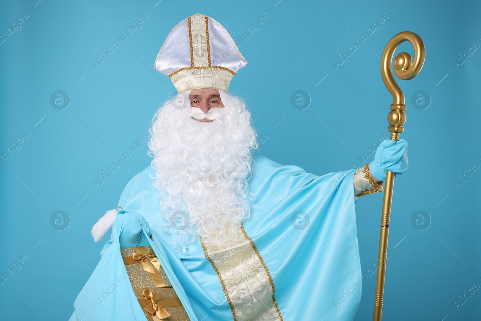 Photo of Saint Nicholas with bag of Christmas gifts and crozier on light blue background