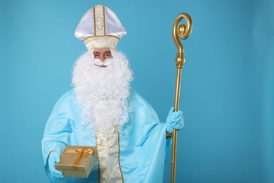 Photo of Saint Nicholas with bag of Christmas gifts and crozier on light blue background