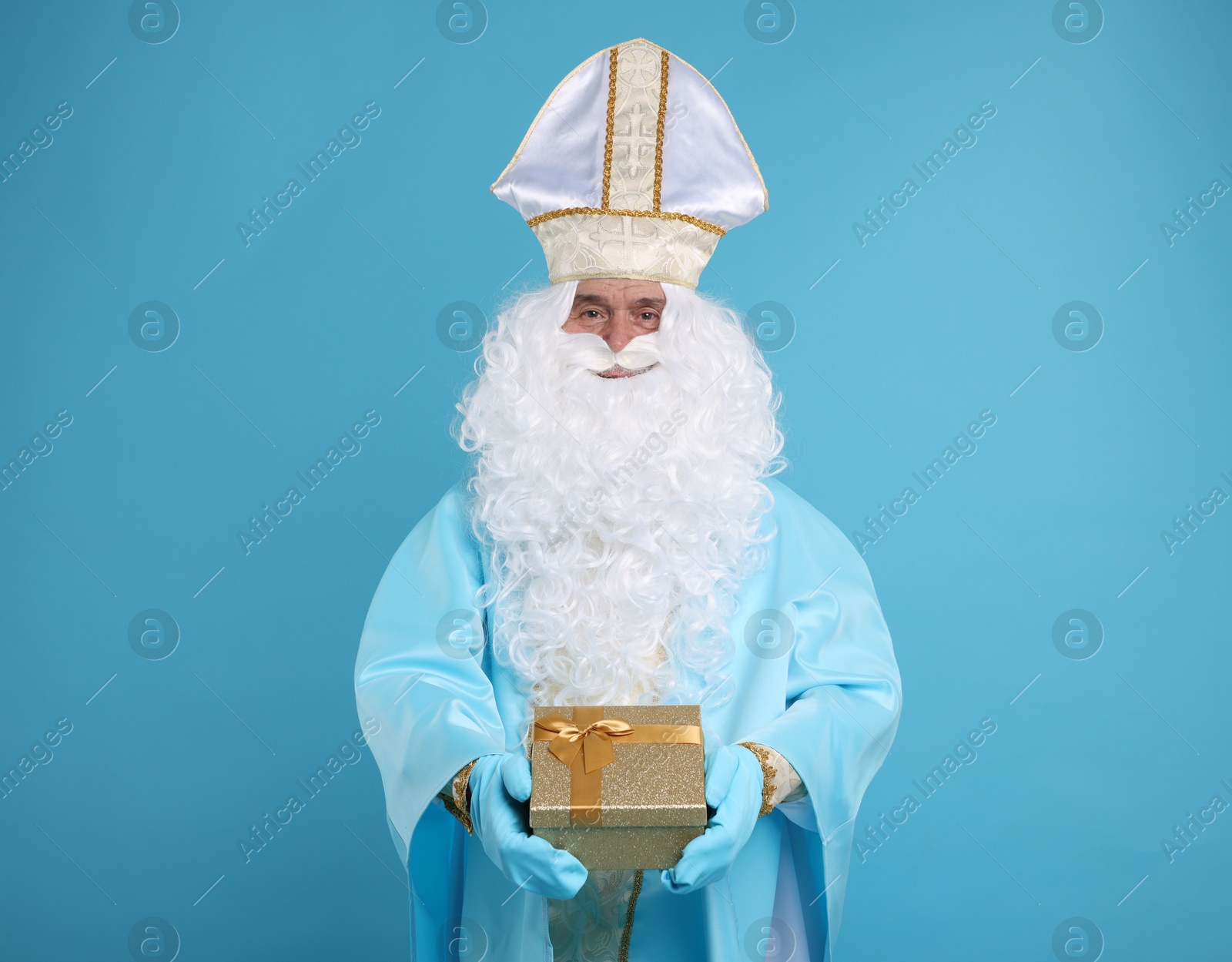 Photo of Saint Nicholas with Christmas gift on light blue background