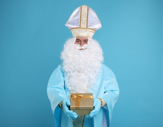 Photo of Saint Nicholas with Christmas gift on light blue background