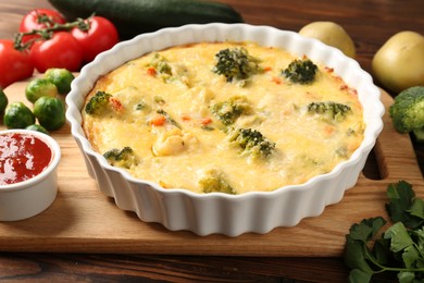 Photo of Delicious vegetable casserole, sauce and ingredients on wooden table, closeup