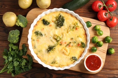 Photo of Delicious vegetable casserole, sauce and ingredients on wooden table, flat lay