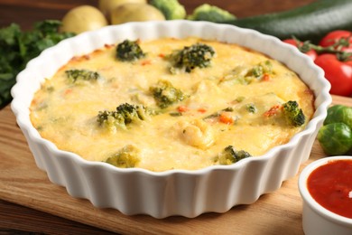 Photo of Delicious vegetable casserole, sauce and ingredients on wooden table, closeup