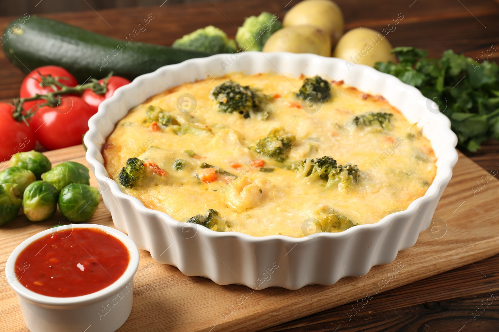 Photo of Delicious vegetable casserole, sauce and ingredients on wooden table, closeup