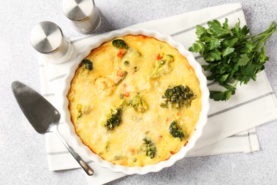 Photo of Delicious vegetable casserole, server, spices and parsley on light table, top view