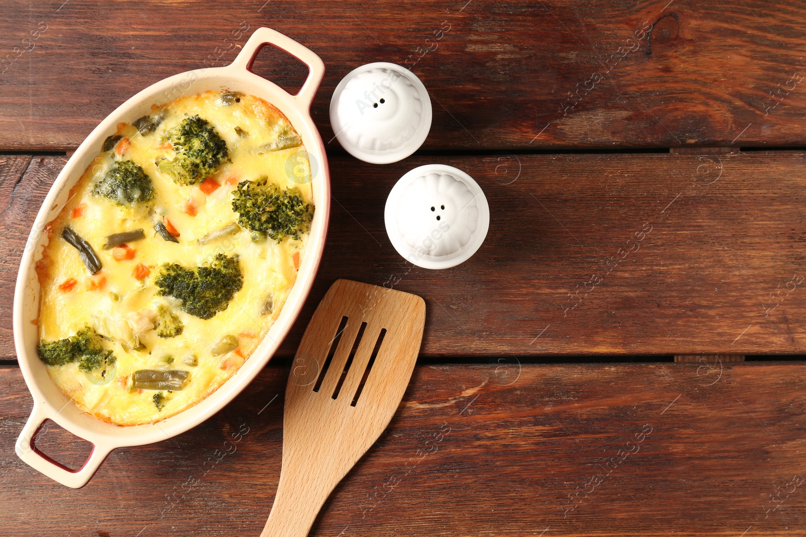 Photo of Delicious vegetable casserole, spices and turner on wooden table, top view. Space for text