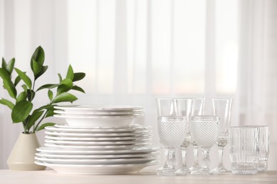 Photo of Empty clean glasses, plates and green branches on table indoors