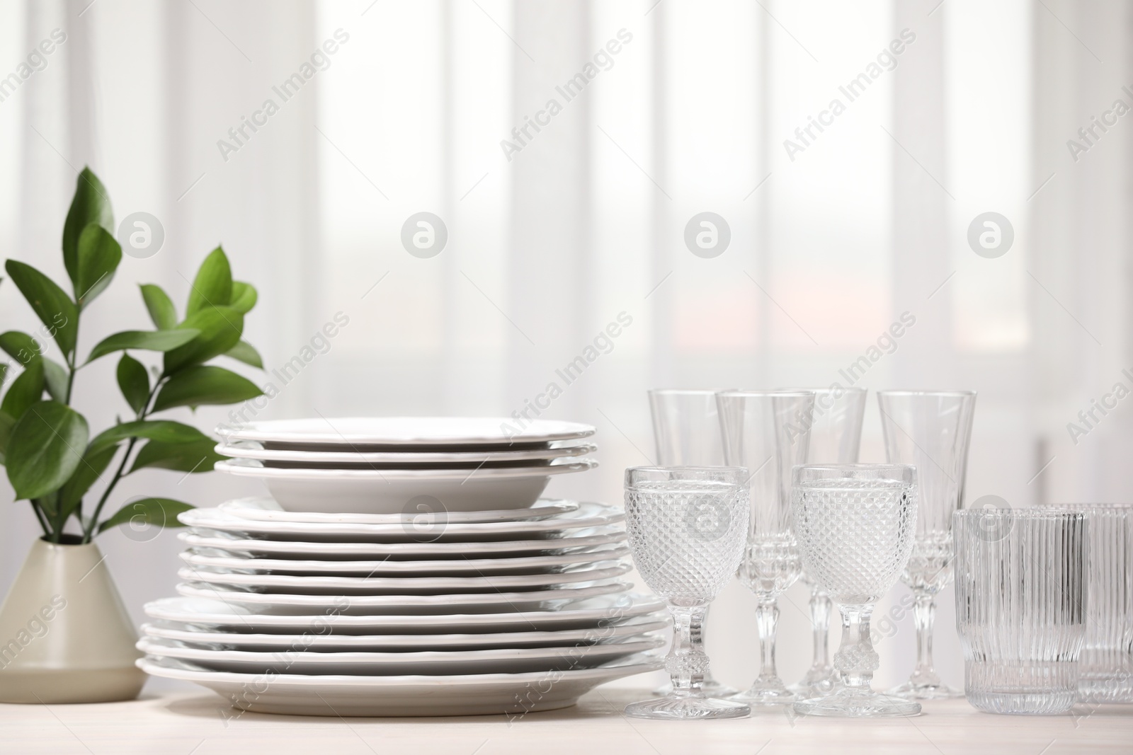 Photo of Empty clean glasses, plates and green branches on table indoors