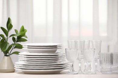 Photo of Empty clean glasses, plates and green branches on table indoors