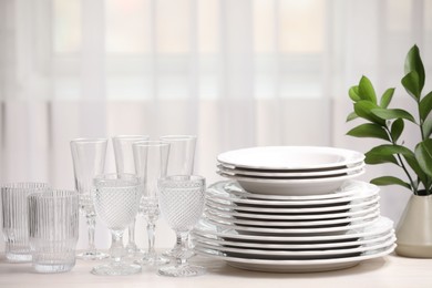 Photo of Empty clean glasses, plates and green branches on table indoors