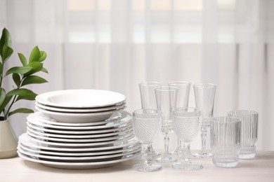 Photo of Empty clean glasses, plates and green branches on table indoors