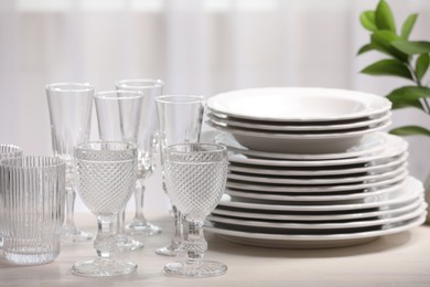 Photo of Empty clean glasses, plates and green branch on table indoors