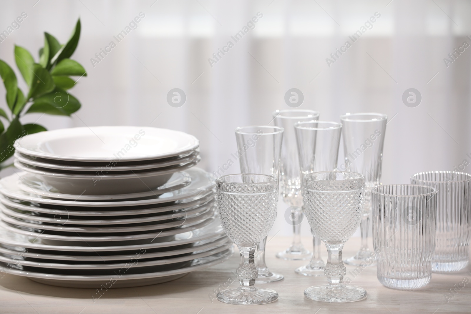 Photo of Empty clean glasses, plates and green branch on table indoors