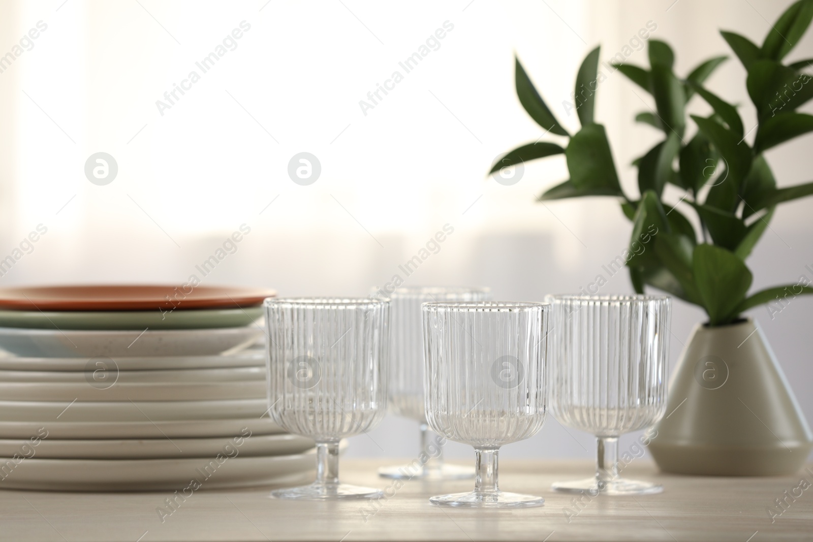 Photo of Empty clean glasses, plates and green branches on table indoors