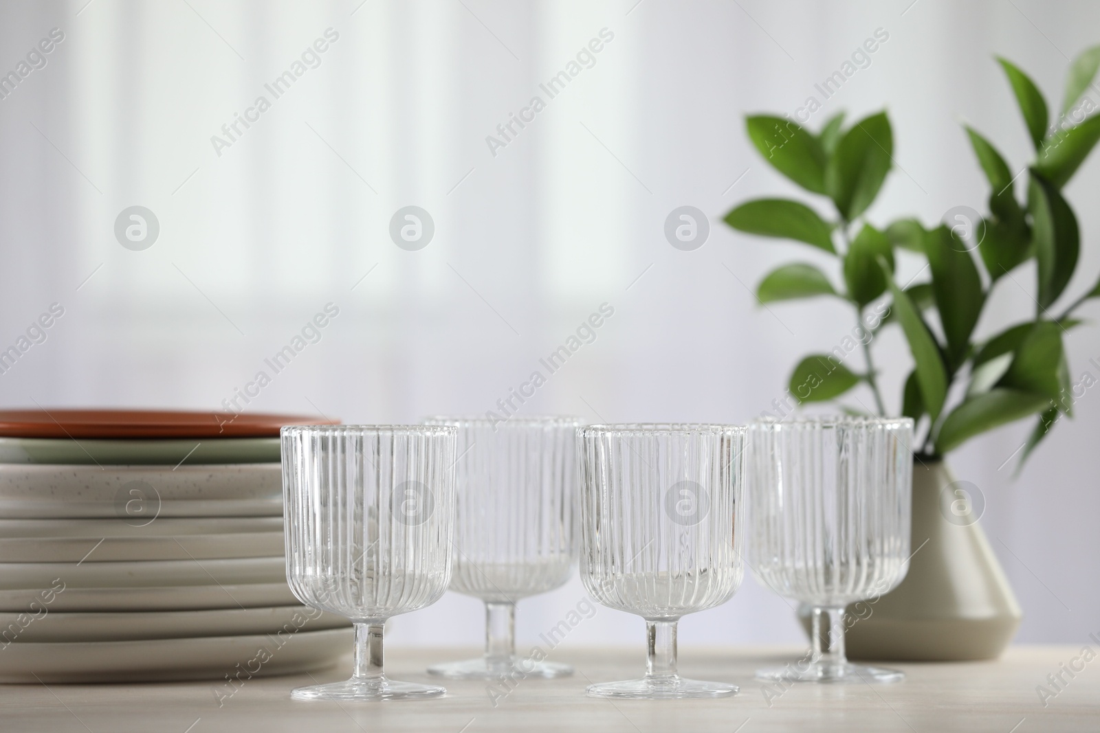 Photo of Empty clean glasses, plates and green branches on table indoors