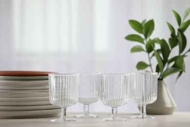 Photo of Empty clean glasses, plates and green branches on table indoors