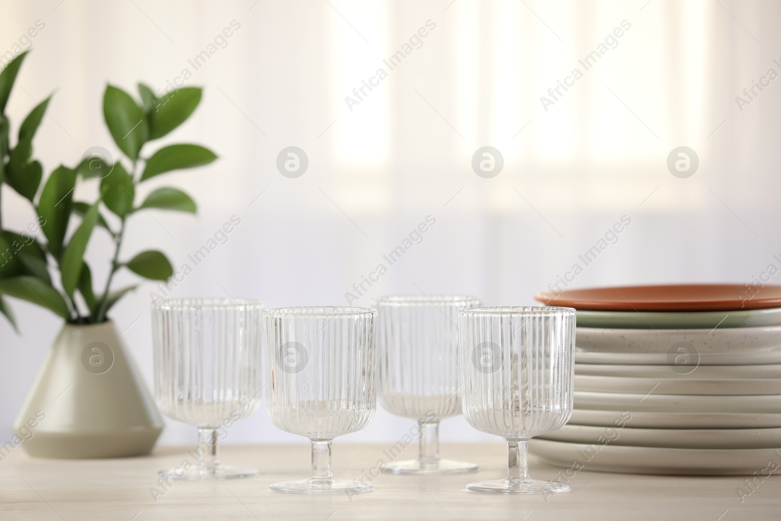 Photo of Empty clean glasses, plates and green branches on table indoors