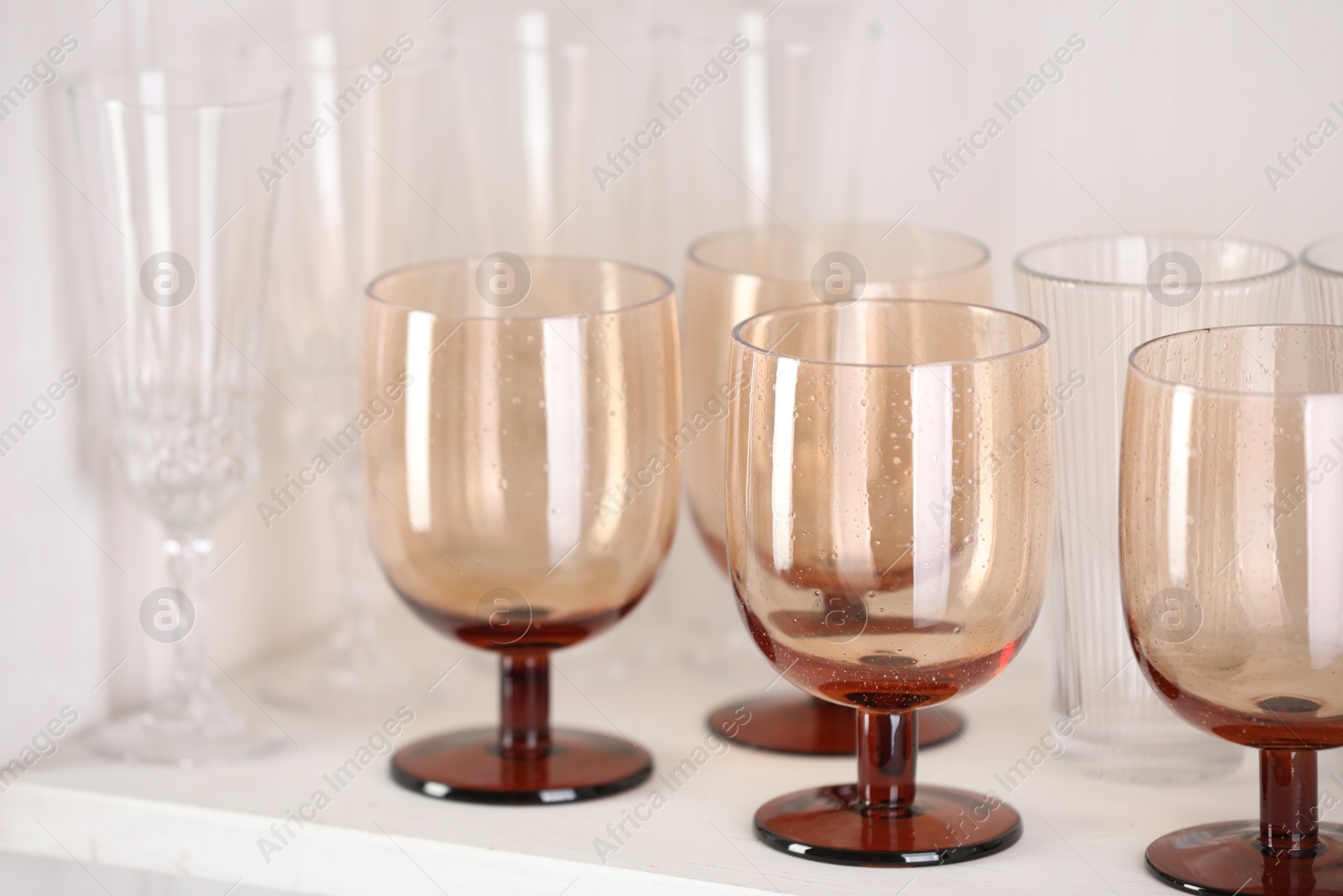 Photo of Different empty clean glasses on white shelf, closeup