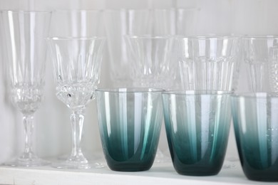 Photo of Different empty clean glasses on white shelf, closeup