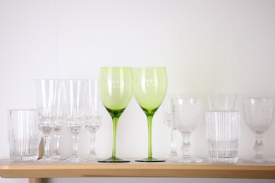 Photo of Empty clean glasses on wooden shelf near white wall indoors