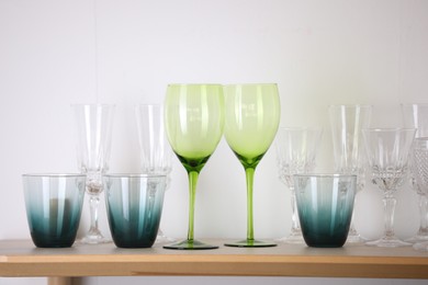 Photo of Empty clean glasses on wooden shelf near white wall indoors