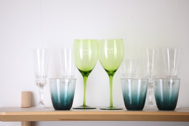 Photo of Empty clean glasses on wooden shelf near white wall indoors