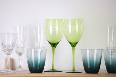 Photo of Empty clean glasses on wooden shelf near white wall indoors